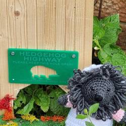 A toy hedgehog outside a labelled hedgehog highway sign